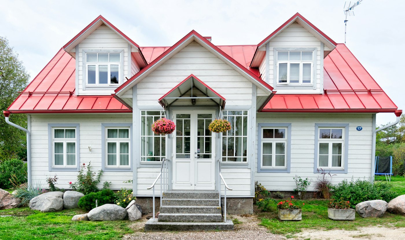 A white timber house with a red metal roof, flower baskets, and steps up to a white front door